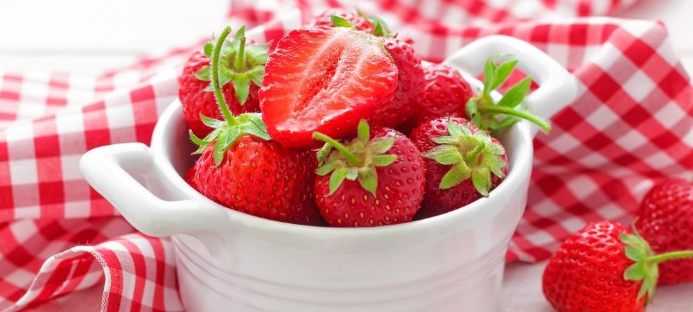 草莓放在一个白色的碗里，上面有格子桌布